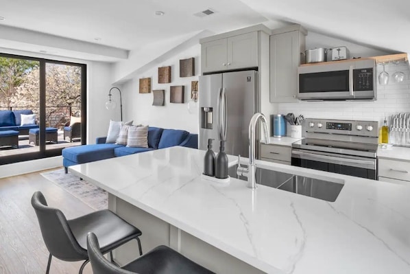 Una cocina moderna con una isla grande, electrodomésticos de acero inoxidable y una zona de estar con un sofá azul.