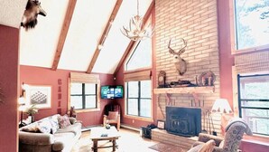 Een ruime woonkamer met een hoge plafond, houten balken, een open haard en een televisie.