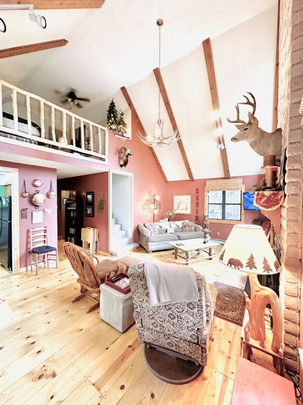 A spacious loft with a high ceiling, exposed wooden beams, a cozy seating area with patterned furniture, and a rustic decor including a deer head and a Christmas tree. - Cabin right next to Burro St. in Cloudcroft (Cloudcroft)