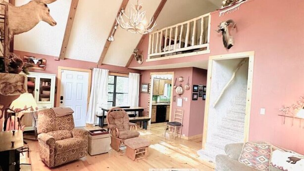 Een ruime woonkamer met hoge plafonds, houten balken, een kroonluchter en rustieke decoratie, waaronder opgeplakte dierenkoppen.