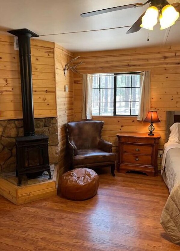 Une chambre confortable dans un chalet, avec une cheminée en pierre, un fauteuil en cuir, une table de chevet en bois avec une lampe et une fenêtre avec des rideaux.