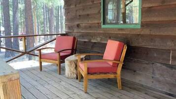 Une terrasse en bois avec deux chaises rouges et une table, une fenêtre avec des bordures vertes, et une vue sur les arbres.