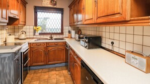 A kitchen with wooden cabinets, a window with a view, a toaster, and a radio. - Llys-yr-onnen (Carmarthen)