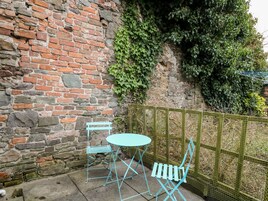 Un muro de ladrillo con una mesa y sillas de metal, un muro de piedra y una cerca verde.