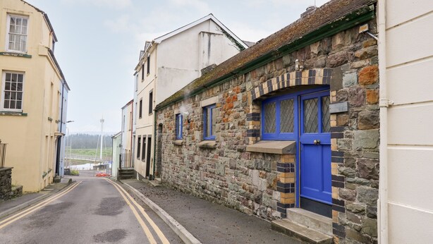 A narrow street with stone buildings, a blue door, and a yellow double line on the road. - Llys-yr-onnen (Carmarthen)
