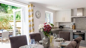 A dining area with a table set for four, a vase of flowers, and a kitchen in the background. - Stop Tide (Port Isaac)