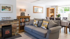A cozy living room with a fireplace, a sofa, a bookshelf, and a dining area with a table set for two. - Stop Tide (Port Isaac)