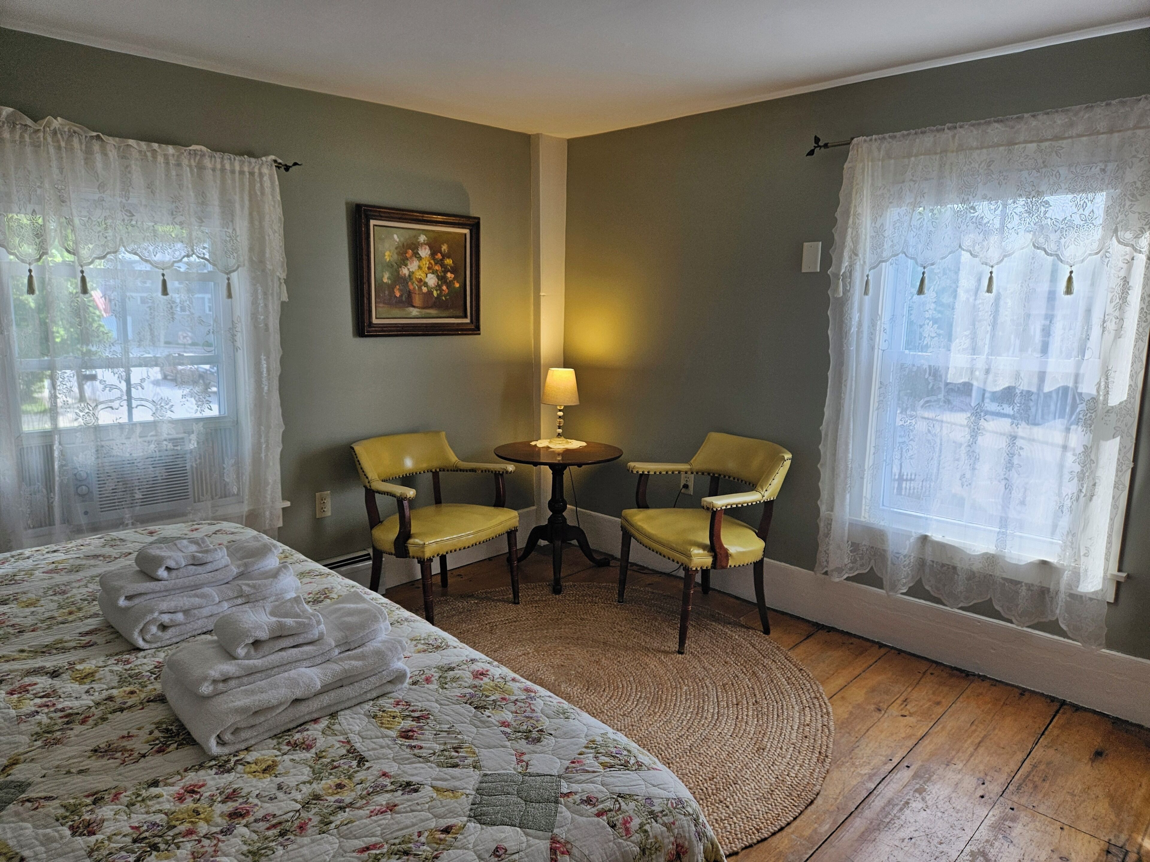 A hotel room with a bed, two chairs, a small table, and a painting on the wall.