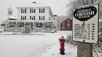 A snow-covered scene with a sign welcoming to Cornish, Maine, listing nearby towns and their distances.