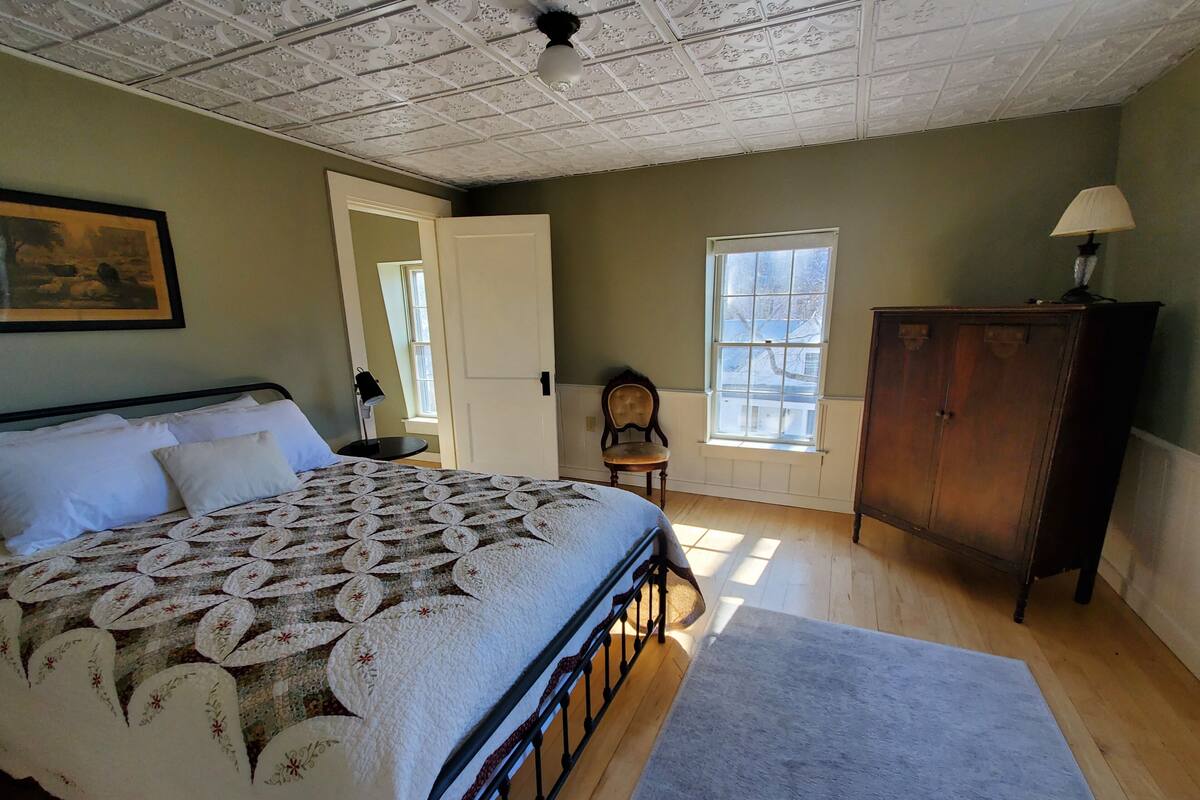 A bedroom with a bed, a wooden cabinet, a chair, and a window.