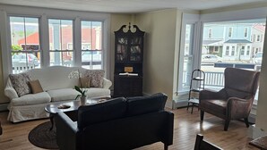 A living room with a white sofa, a black leather chair, a wooden coffee table, and a bookshelf. - The Cornish Inn (Cornish)