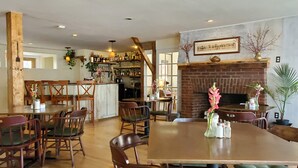 A restaurant with wooden furniture, a brick fireplace, and a bar area with shelves of bottles. - The Cornish Inn (Cornish)