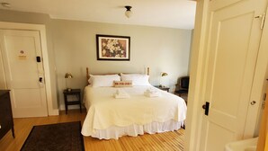 A neatly arranged bedroom with a bed, bedside tables, a nightstand, a wall-mounted picture, and a door. - The Cornish Inn (Cornish)