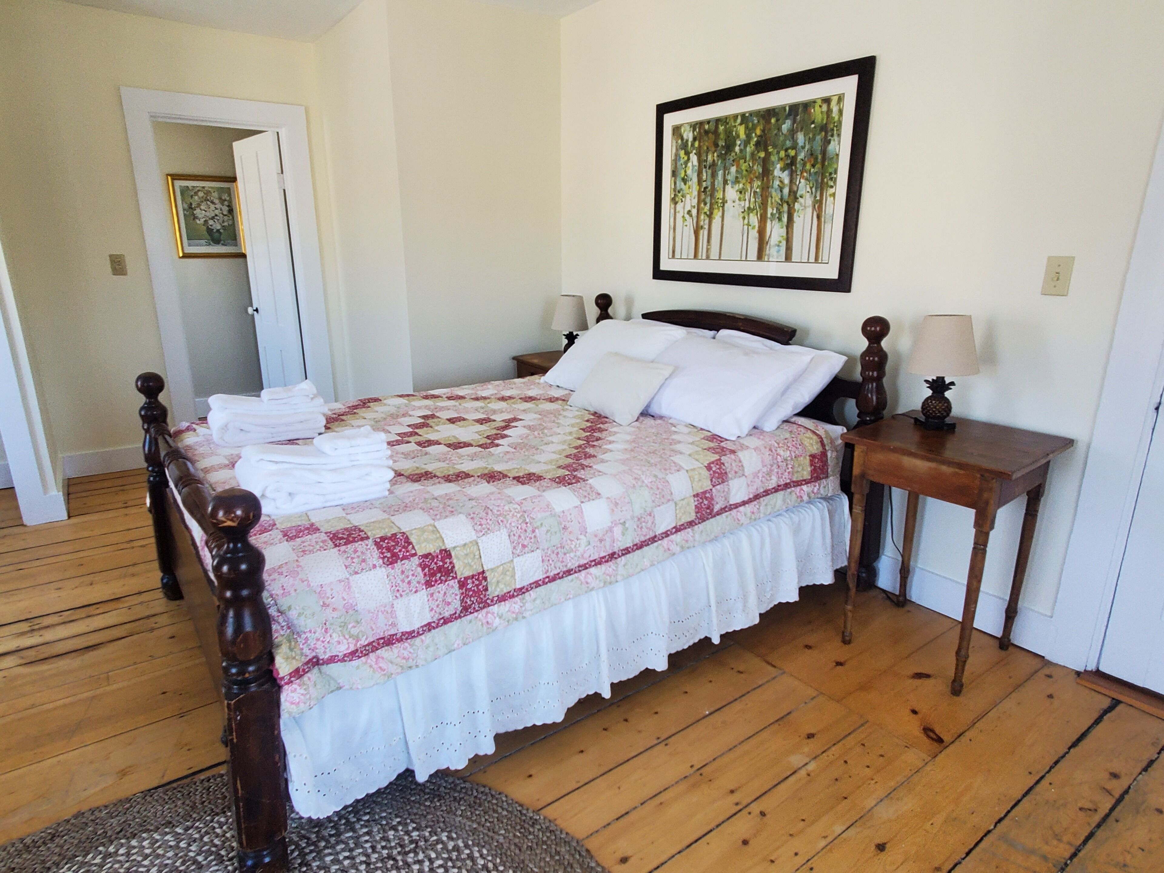 A neatly made bed with a floral quilt, wooden headboard, two bedside tables with lamps, and a framed painting on the wall.