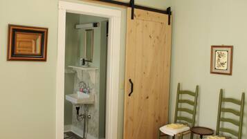 A bathroom with a sink, mirror, and a wooden door. There are two chairs and a small table.