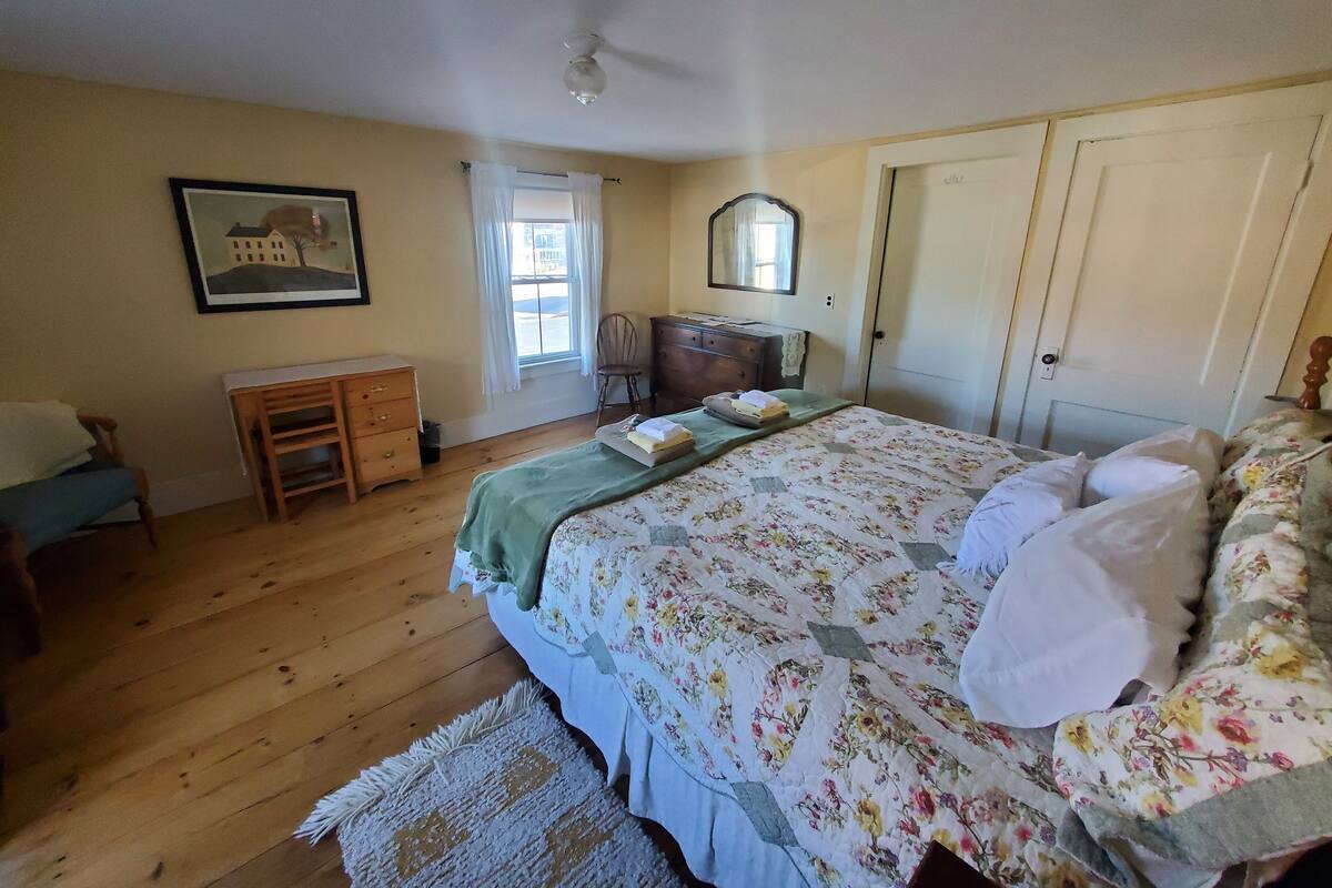 A bedroom with a bed, dresser, chair, and a painting on the wall.