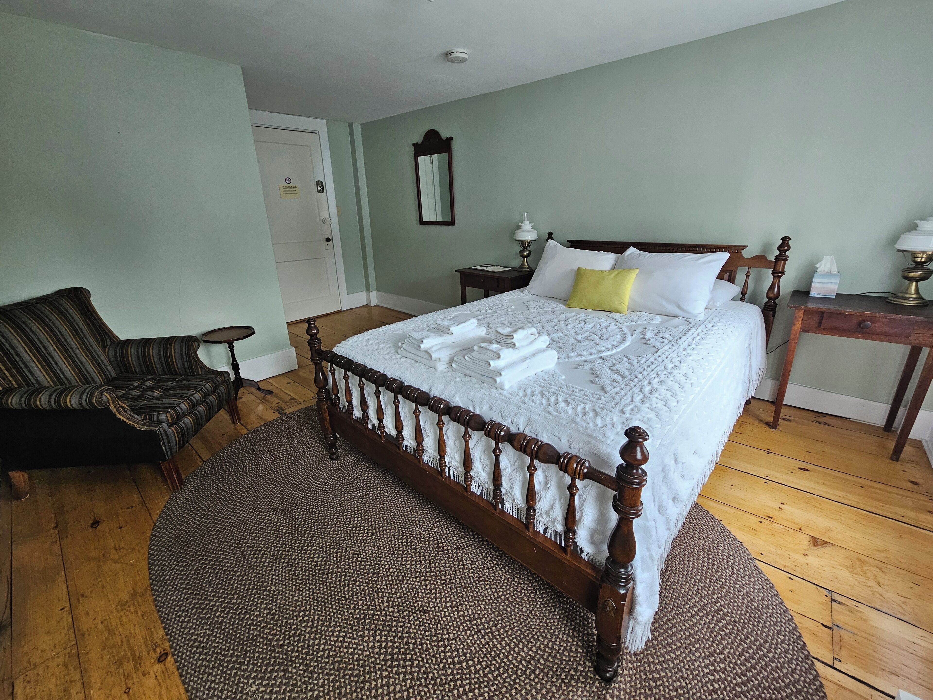 A neatly arranged bedroom with a large bed, a chair, a bedside table, and a door.