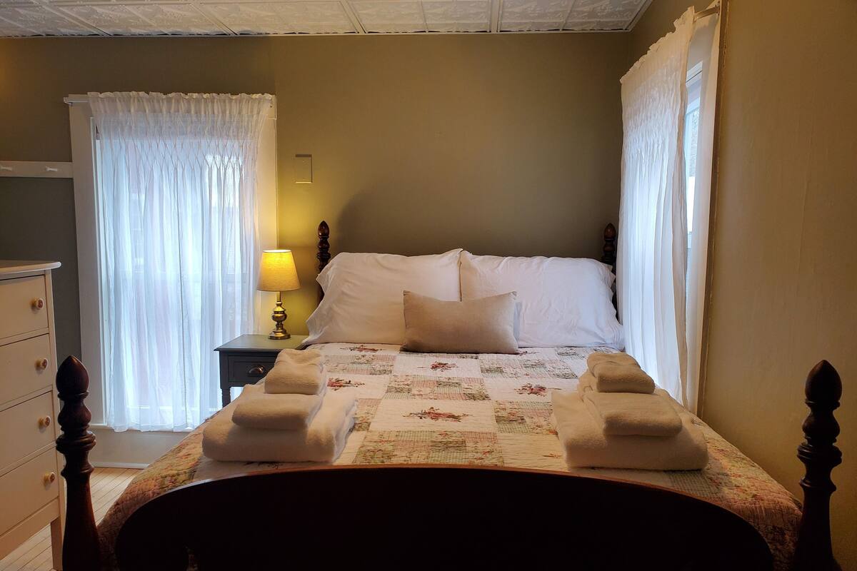 A neatly made bed with a floral quilt, a bedside lamp, and a wooden nightstand.
