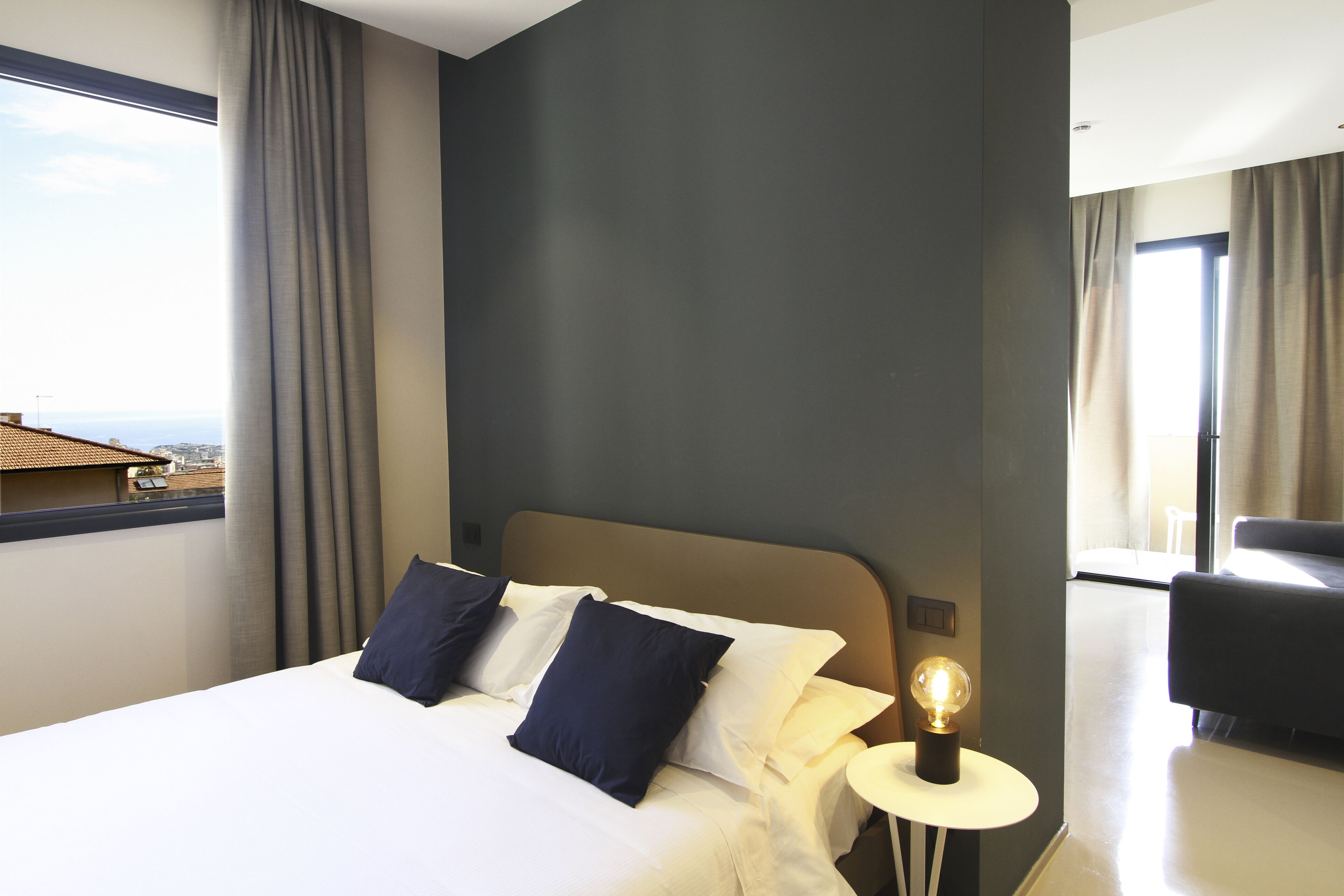 A hotel room with a bed, a bedside lamp, and a view of the cityscape.