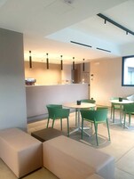 Un interno moderno e minimalista con sedie verdi e un divano bianco, un bancone con un computer e una finestra che offre luce naturale.