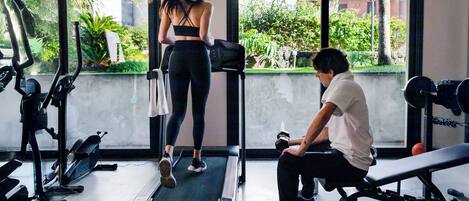 A gym with exercise equipment, a treadmill, and a person using a bench.