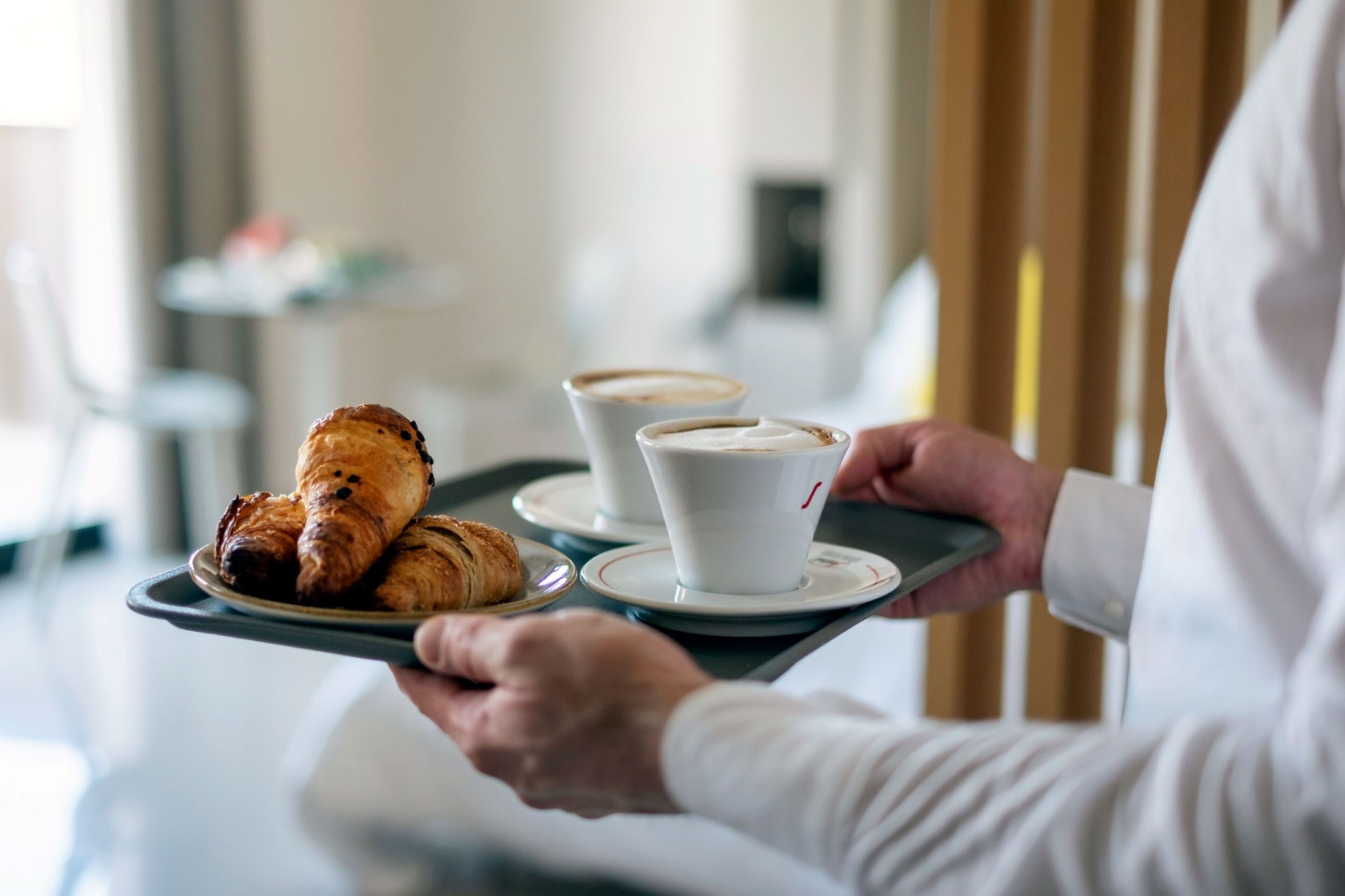 A tray with croissants and two cups of coffee, held by a person in a white shirt.