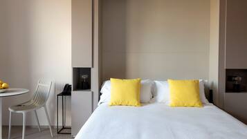 Quarto de hotel com cama, duas almofadas, uma cadeira, uma mesa pequena e um telefone em suporte.