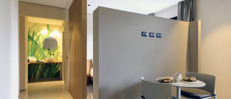 Ein modernes Hotelzimmer mit Essbereich, inklusive Tisch, einer Platte mit Keksen, einer Tasse, einem Stuhl und einer Wand mit Pflanzenmotiv.