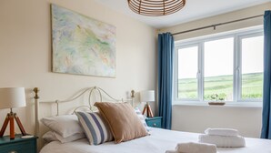 En pænt redt seng med puder, et natbord med lampe, og udsigt til det fri gennem et vindue.