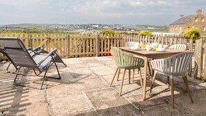En terrasse med et bord og stole, et træhegn og udsigt til en bygning i sten samt landskab.