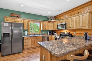 A kitchen with wooden cabinets, a granite countertop, a stainless steel refrigerator, and a microwave.