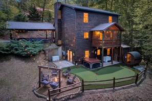 A two-story wooden cabin with a deck, outdoor seating, and a small putting green.