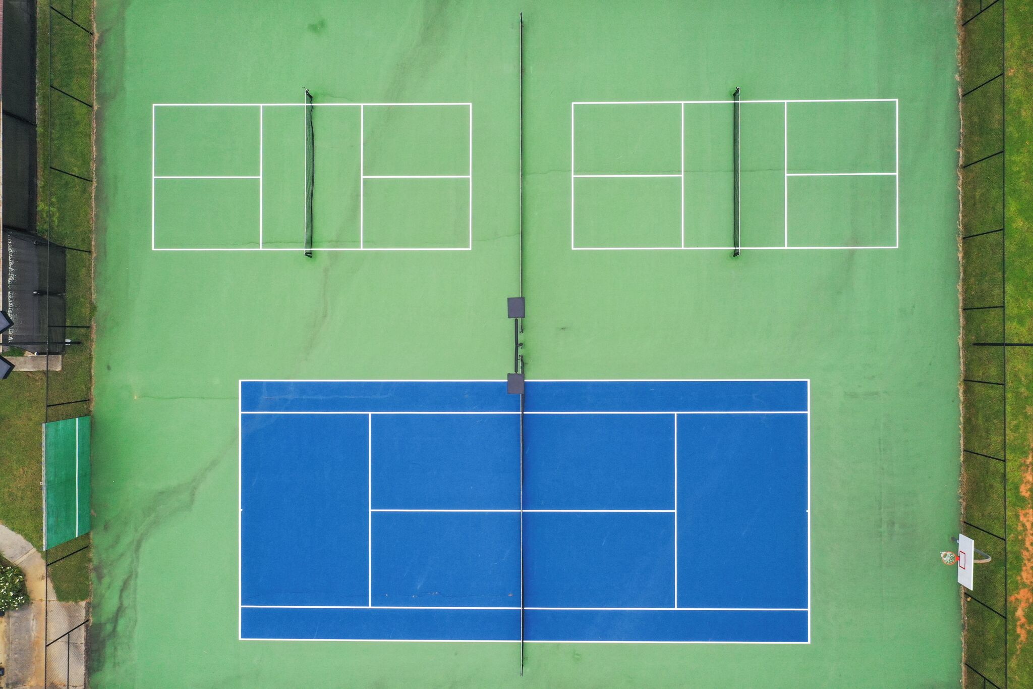 An aerial view of a tennis court with two smaller courts and a larger court, surrounded by a fence.