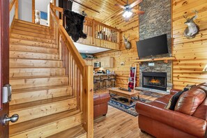 A wooden interior with a staircase, a fireplace, a leather sofa, and a mounted deer head.