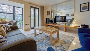 A modern living room with a sofa, coffee table, TV, and a dining area with a table and chairs. - Riverside Park 2 (Keswick)