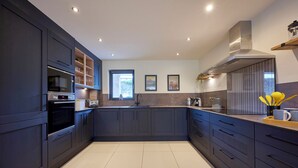 A modern kitchen with dark cabinetry, a built-in oven, and a large island with a sink. - Riverside Park 2 (Keswick)
