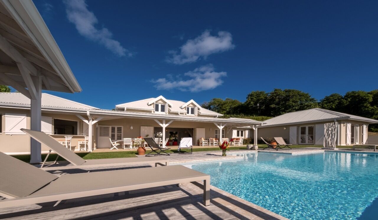 Un espace aménagé au bord de la piscine, avec des chaises longues, un patio couvert et une grande maison en arrière-plan.