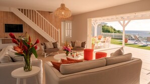 A modern living room with a staircase, a dining area, and a patio with outdoor seating. - Petite Grenade - View, sea access, infinity pool and tennis court (Le Vauclin)