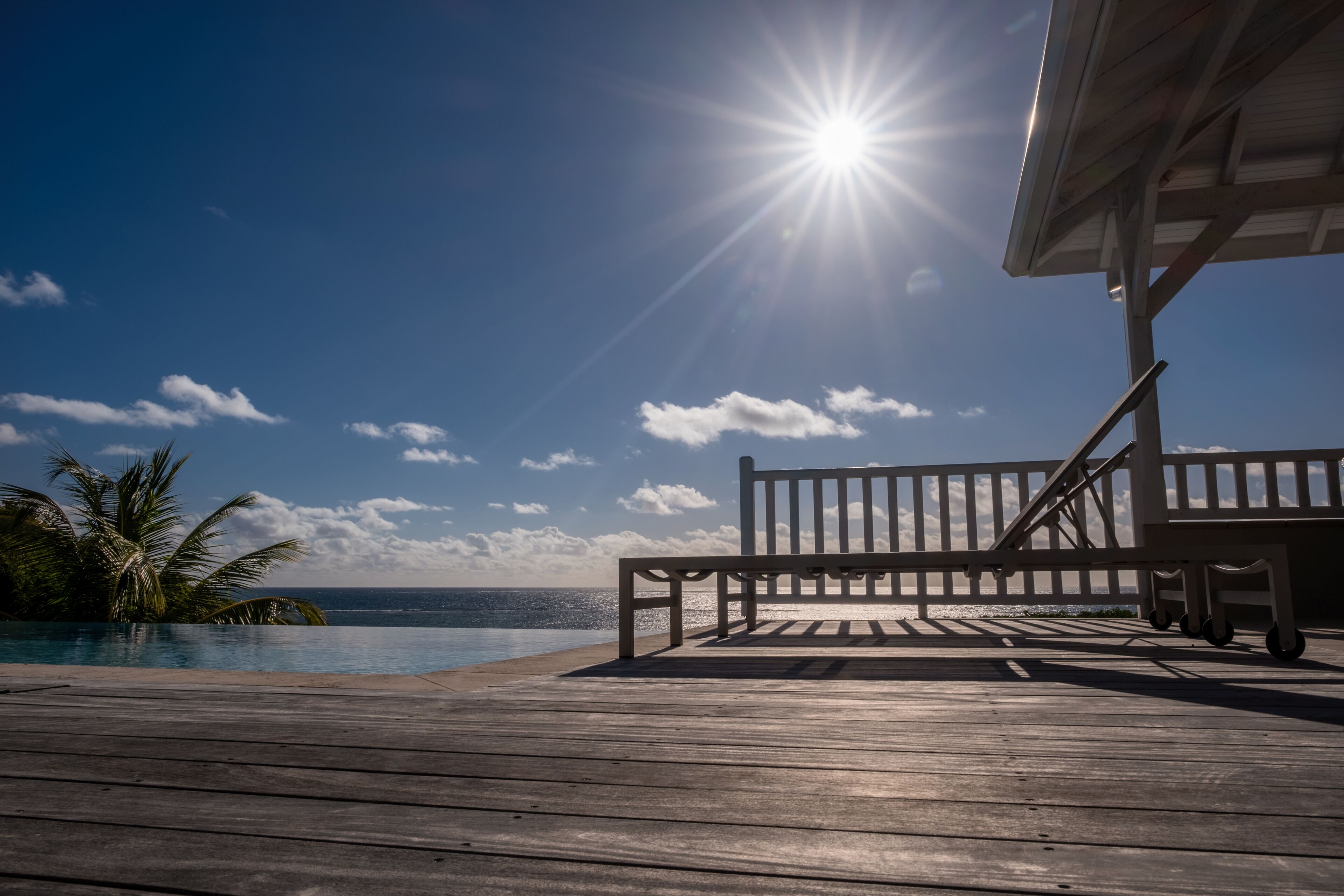 Eine Holzterrasse mit einer Bank, die einen Blick auf ein Schwimmbad und den Ozean bietet.