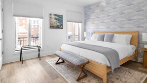 A bedroom with a bed, bench, and large windows.