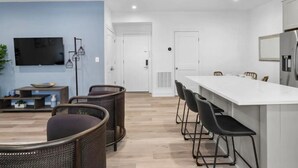 A modern kitchen with a white countertop, bar stools, and a flat-screen TV mounted on the wall.