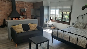 A cozy living room with a sofa, a small table, a bed, a fireplace, and a kitchen area. - HOUSE/LOFT WITH SEA VIEWS, LARGE SWIMMING POOL, VERY QUIET. 2.5 KM FROM THE BEACH (Canet de Mar)