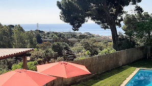 A backyard with a swimming pool, two red umbrellas, and a table with chairs. - HOUSE/LOFT WITH SEA VIEWS, LARGE SWIMMING POOL, VERY QUIET. 2.5 KM FROM THE BEACH (Canet de Mar)