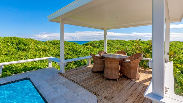Ein überdachter Außenbereich mit Pool, Korbmöbeln und Blick auf das Meer und die grüne Landschaft.