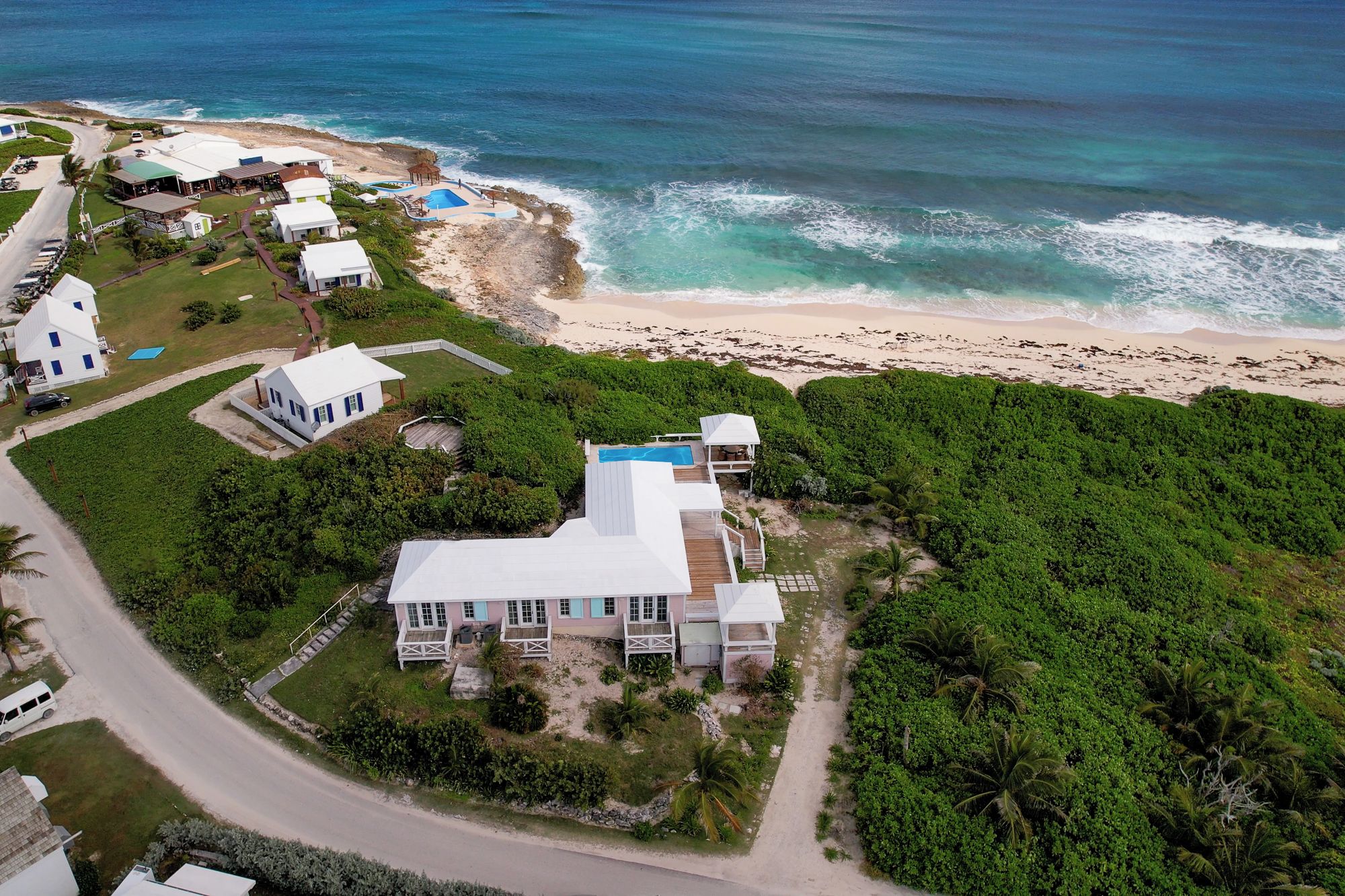 An aerial view of a coastal property with a large house, a swimming pool, and a beach.