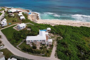 An aerial view of a coastal property with a large house, a swimming pool, and a beach.