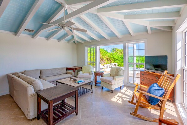 A spacious living room with a high ceiling, a ceiling fan, a sofa, a coffee table, a TV, and a rocking chair.