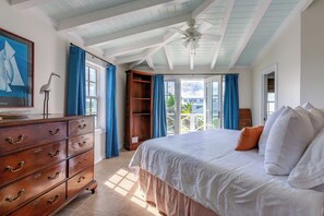 Un dormitorio con una cama grande, un aparador, un ventilador de techo y vistas al exterior.