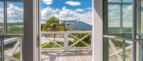 A view from a balcony with a wooden deck, overlooking a building with a blue roof and a white fence.