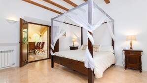 Una camera da letto con un letto a baldacchino, un comodino in legno, una lampada e vista su un patio esterno.